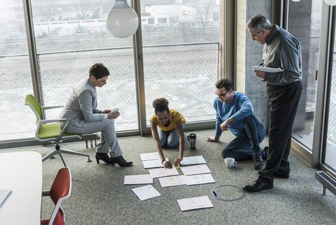 Businesspeople looking at documents on office floor - UUF10016