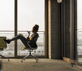 Businesswoman sitting on office chair using cell phone - UUF10031