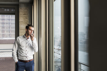 Junger Geschäftsmann benutzt Handy am Fenster - UUF10054