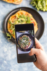 Hand eines Mädchens, das eine hausgemachte vegetarische Pizza mit dem Handy fotografiert, Nahaufnahme - SARF03218