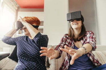 Adult daughter with mother at home wearing VR glasses - ZEDF00533