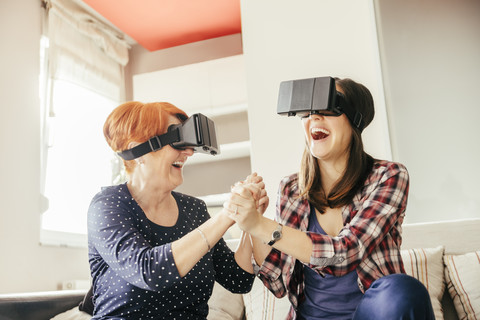 Aufgeregte erwachsene Tochter mit Mutter zu Hause mit VR-Brille, lizenzfreies Stockfoto