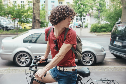 Junger Mann fährt Fahrrad auf dem Bürgersteig und dreht sich um, lizenzfreies Stockfoto