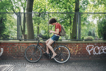 Junger Mann, der auf seinem Fahrrad sitzend ein Mobiltelefon benutzt - RTBF00709
