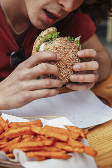 Junger Mann isst veganen Hamburger und Süßkartoffelpommes - RTBF00715