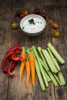 Schale mit Kräuter-Joghurt-Dip, Kirschtomaten und verschiedenen Gemüsesticks auf Holz - LVF05919