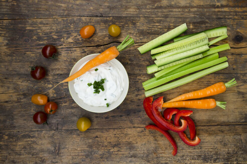 Schale mit Kräuter-Joghurt-Dip, Kirschtomaten und verschiedenen Gemüsesticks auf Holz - LVF05920