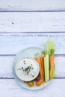 Schale mit Kräuter-Joghurt-Dip, Kirschtomaten und Gemüsesticks auf dem Teller - LVF05924