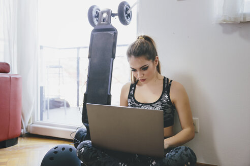 Young woman using laptop while electric skateboard is chragig - LCUF00103