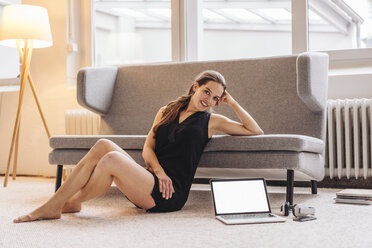 Portrait of smiling woman leaning on couch next to laptop - JOSF00622