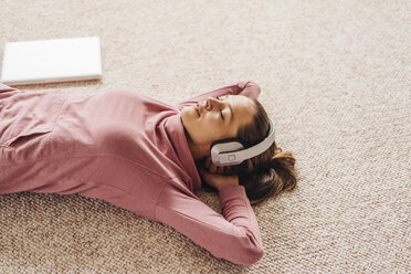 Woman lying on carpet wearing headphones - JOSF00633