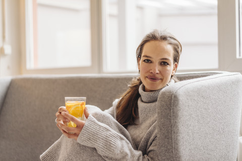 Porträt einer Frau, die auf einer Couch sitzt und ein frisches Getränk hält, lizenzfreies Stockfoto