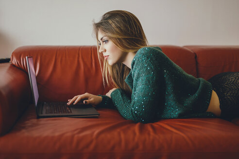 Young woman lying on the couch using laptop - LCUF00105