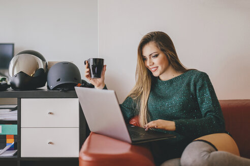 Young woman relaxing on the couch with cup of coffee using laptop - LCUF00109