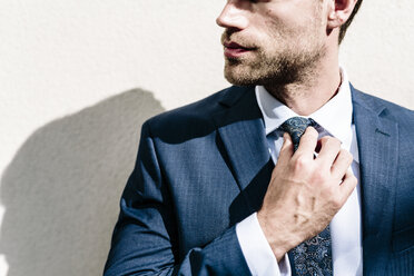 Handsome businessman fixing his tie, standing in front of white wall - GIOF02041