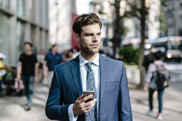 Gutaussehender Geschäftsmann, der in Manhattan spazieren geht und ein Mobiltelefon benutzt - GIOF02046