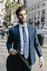 Gutaussehender Geschäftsmann, der in Manhattan spazieren geht und eine Jacke auf einem Bügel trägt - GIOF02048