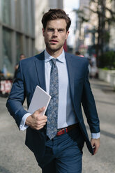 Handsome businessman walking in Manhattan, carrying digital tablet - GIOF02050