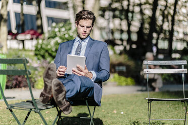 Geschäftsmann in Manhattan, der auf einem Gartenstuhl sitzt und ein digitales Tablet mit hochgelegten Füßen benutzt - GIOF02062