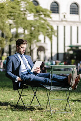Geschäftsmann in Manhattan, der auf einem Gartenstuhl sitzt und ein digitales Tablet mit hochgelegten Füßen benutzt - GIOF02063
