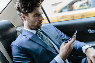 Businessman sitting in taxi, using smart phone - GIOF02083