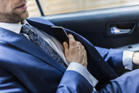 Geschäftsmann sitzt im Taxi und benutzt ein Smartphone, lizenzfreies Stockfoto