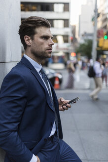 Businessman leaning on a wall in the city, using smart phone - GIOF02091