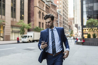 Alleinstehender Geschäftsmann in Eile, der durch Manhattan läuft und sein Smartphone benutzt - GIOF02095