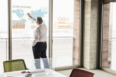 Businessman touching windowpane with world map and global network in office - UUF10057