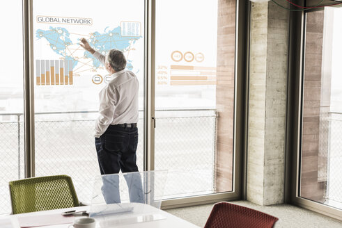 Geschäftsmann berührt Fensterscheibe mit Weltkarte und globalem Netzwerk im Büro - UUF10057