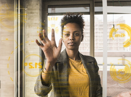 Young woman touching glass wall with data in office - UUF10059
