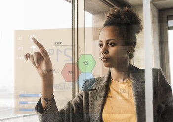 Young woman touching glass wall with data in office - UUF10060