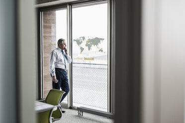 Businessman looking at windowpane with world map in office - UUF10064