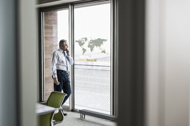 Geschäftsmann schaut auf Fensterscheibe mit Weltkarte im Büro - UUF10064