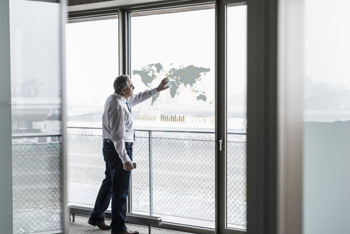 Geschäftsmann berührt Fensterscheibe mit Weltkarte im Büro - UUF10066