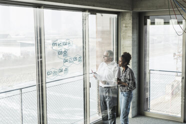 Businessman and woman at windowpane with data in office - UUF10071