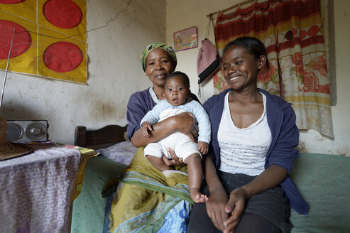 Madagaskar, Fianarantsoa, Baby, Mutter und Großmutter sitzen im Wohnzimmer - FLKF00761