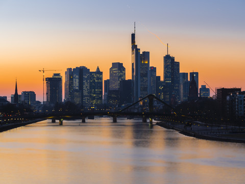 Deutschland, Frankfurt, Blick auf Skyline mit Flößerbrücke und Main im Vordergrund in der Dämmerung, lizenzfreies Stockfoto