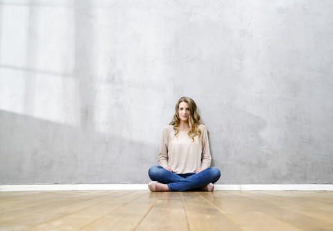Blonde Frau sitzt auf dem Boden vor einer grauen Wand, lizenzfreies Stockfoto