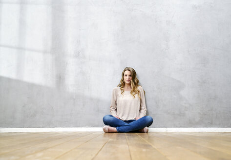 Blond woman sitting on the floor in front of grey wall - FMKF03563