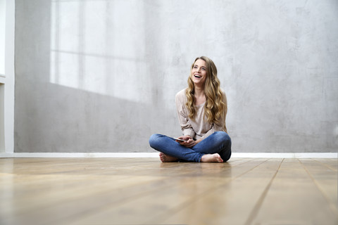 Lachende blonde Frau auf dem Boden sitzend mit Mobiltelefon, lizenzfreies Stockfoto