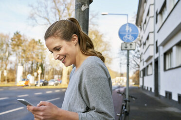 Smiling blond woman looking at cell phone - FMKF03573