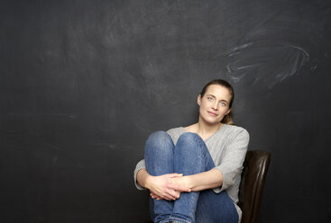 Portrait of smiling woman sitting in front of blackboard - FMKF03577
