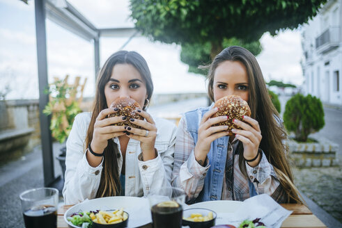 Portrait of two women holding hamburgers in a street restaurant - KIJF01301