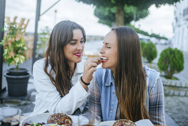 Young woman feeding her friend in a street restaurant - KIJF01304