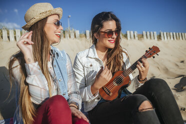 Zwei junge Frauen mit Ukulele sitzen am Strand - KIJF01305