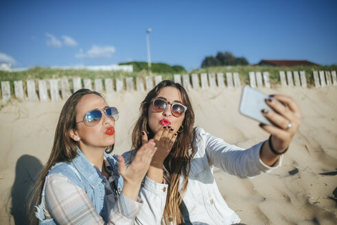 Zwei junge Frauen machen ein Selfie am Strand, während sie sich küssen - KIJF01308