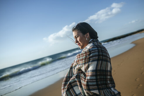 Junge Frau mit Decke am Strand und Blick auf das Meer - KIJF01312