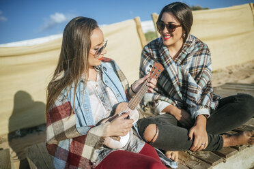 Frau spielt Ukulele am Strand, während ihr Freund sie beobachtet - KIJF01316