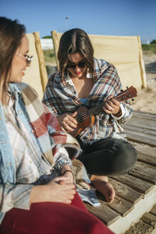 Frau spielt Ukulele am Strand, während ihr Freund sie beobachtet - KIJF01319